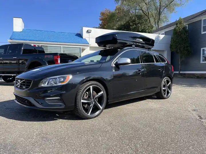 Black Volvo V60 wagon with a roof box in front of the shop's blue roof