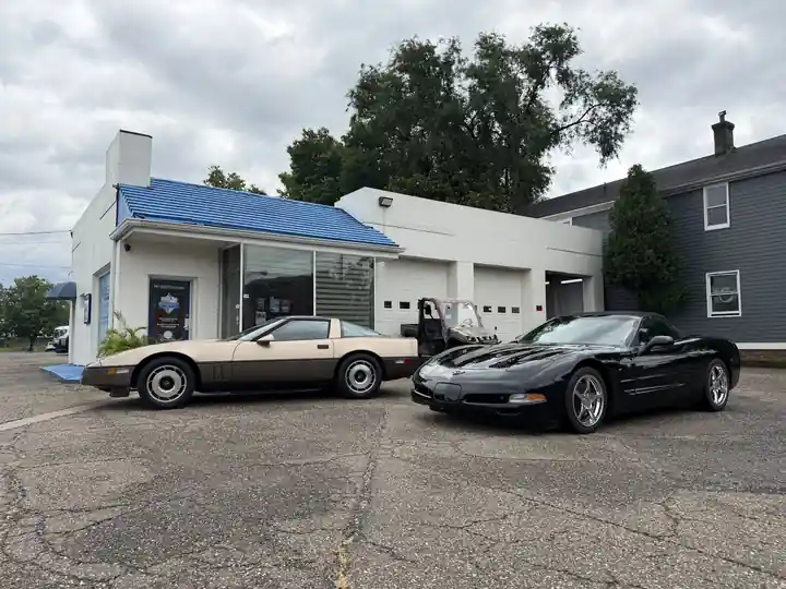 Tan C4 and black C5 convertible Corvettes in front of the shop