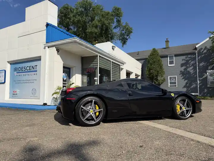Black Ferrari 458 Spider parked beside the white shop under a blue sky