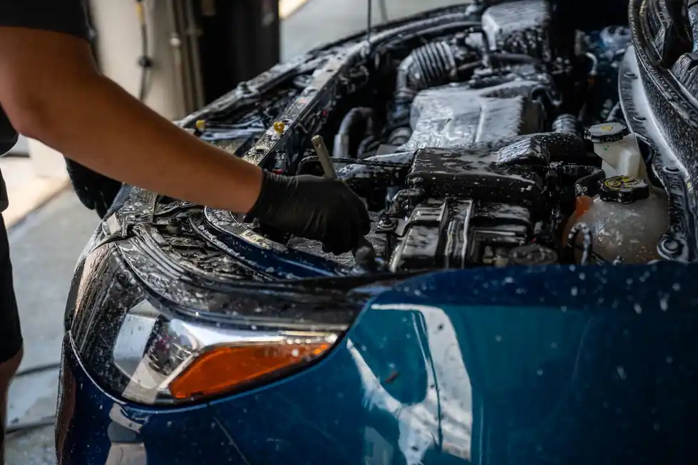 Gloved hand working a wet, foamed engine bay on a blue car